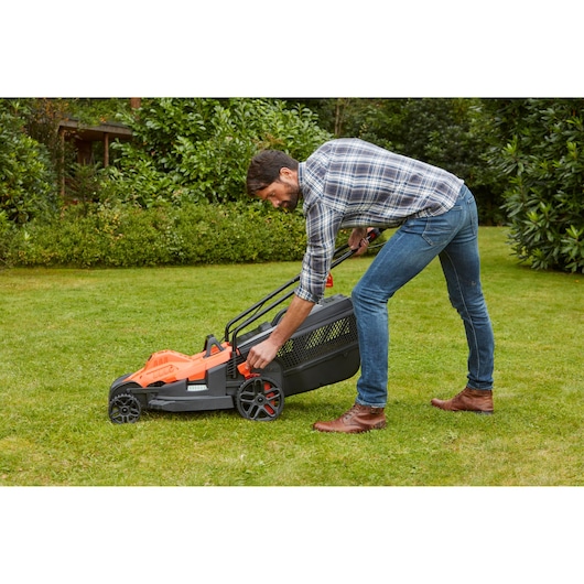 Photo de la tondeuse BLACKDECKER BEMW481BH sur gazon, utilisateur réglant la hauteur.