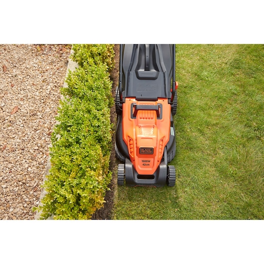 BLACKDECKER BEMW481BH tondeuse électrique vue de dessus, design orange et noir, coupe l’herbe près d’une haie.