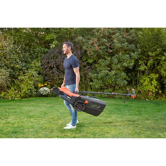 BLACKDECKER BEMW481ES grasmaaier gedragen door een persoon in een tuin, oranje en zwart ontwerp.