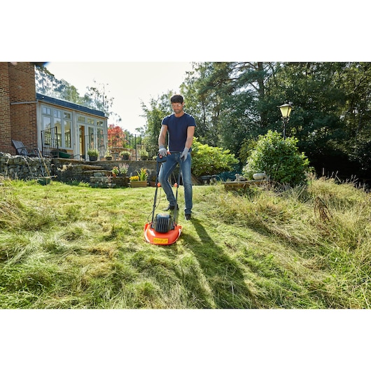 BLACKDECKER BEMWH551 tondeuse à gazon utilisée sur pelouse près de la maison, corps orange et poignée noire.