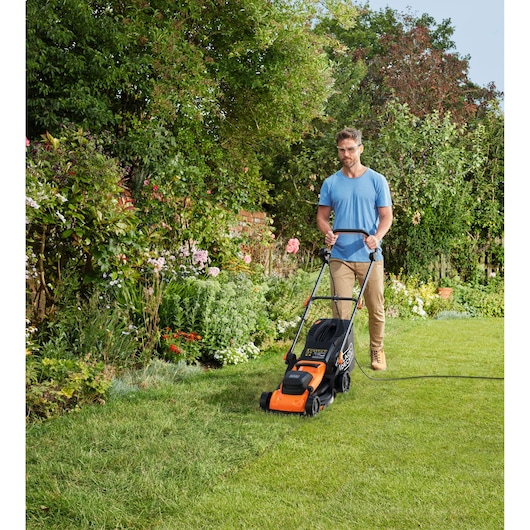 BLACKDECKER BEMWP340-QS tondeuse à gazon orange et noire coupant l’herbe dans un jardin extérieur.
