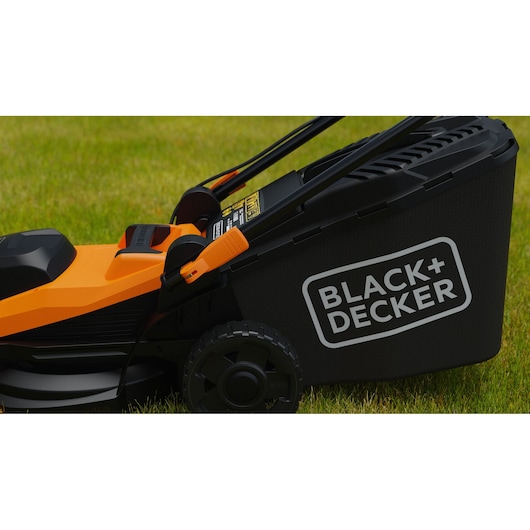 Photo de la tondeuse électrique BLACK+DECKER BEMWP340-QS vue latérale sur gazon, corps noir et orange, bac arrière à herbe.