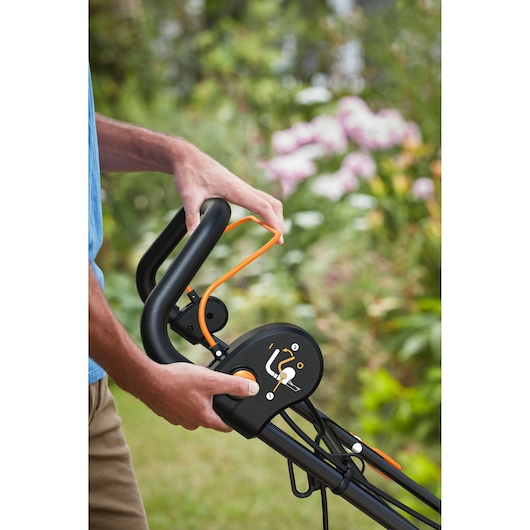 Poignée de tondeuse BLACKDECKER BEMWP340-QS en gros plan, panneau de commande et levier de sécurité orange en extérieur.