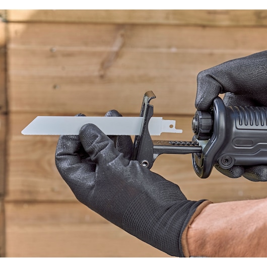 Close-up van een persoon met zwarte handschoenen die een zaagblad in een BLACK+DECKER reciprozaag plaatst, met een houten achtergrond.