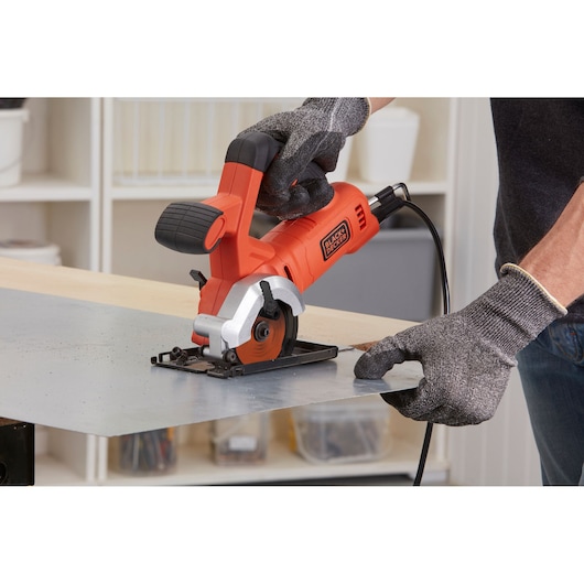 Foto van BLACKDECKER BES510K compacte cirkelzaag die een metalen plaat zaagt in werkplaats, operator met handschoenen.