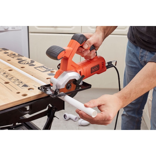 Foto van de BLACKDECKER BES510K compacte cirkelzaag die een witte kunststof buis op een werkbank zaagt.