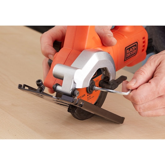 Foto van BLACK+DECKER BES510K compacte cirkelzaag die wordt afgesteld met een inbussleutel op houten oppervlak.