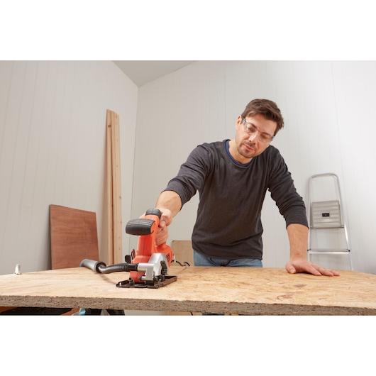 Foto van een persoon die een BLACKDECKER BES510 compacte cirkelzaag gebruikt om hout te zagen op een werkbank.