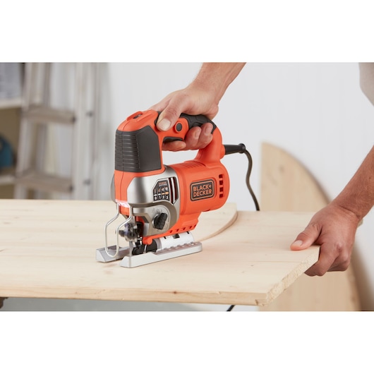 BLACK+DECKER BES610K decoupeerzaag in oranje en zwart zaagt een gebogen lijn in een houten plank.