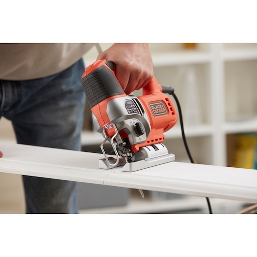 Foto van BLACKDECKER BES610K decoupeerzaag die hout zaagt, close-up met oranje en zwarte behuizing.