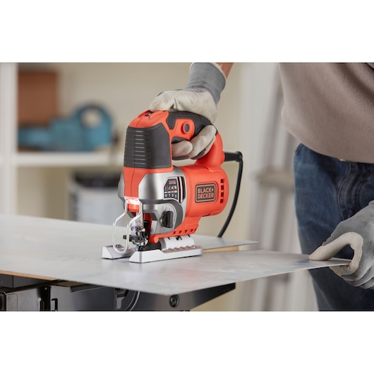 Foto van BLACK+DECKER BES610K decoupeerzaag in gebruik, snijdt een metalen plaat, bediener draagt handschoenen.