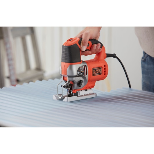 BLACK+DECKER BES610K decoupeerzaag in gebruik op golfplaat, fotografie van oranje en zwart ontwerp.