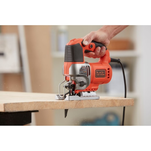 Foto van BLACK+DECKER decoupeerzaag BES610K in gebruik, houtzagen, ergonomische handgreep, oranje en zwart design.