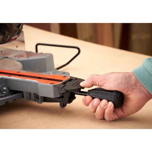 Close-up foto van hand die BLACK+DECKER BES701 verstekzaag afstelt met zwart handvat op houten werkbank.