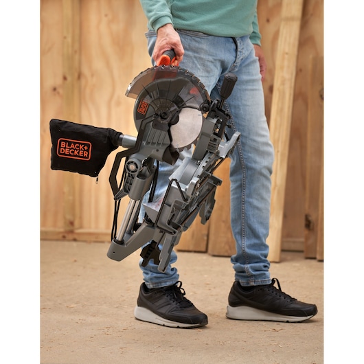 Foto van een persoon die een BLACK+DECKER BES701 verstekzaag aan het handvat vasthoudt op een werkplaatsvloer.