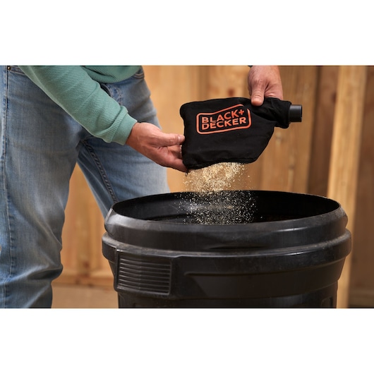 Foto van persoon die stof uit de BLACK+DECKER BES701 stofzak in een zwarte container leegt.