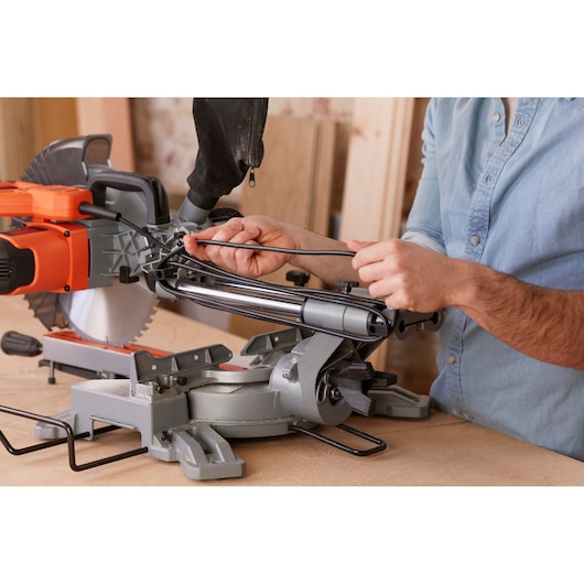 Photo de scie à onglet BLACKDECKER BES710 sur établi, personne ajustant le cordon d’alimentation, vue latérale rapprochée.