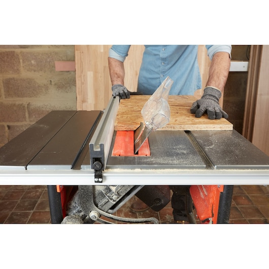 BLACKDECKER BES720 tafelzaag in gebruik met het zagen van een houten paneel, handschoenen zichtbaar, binnenwerkplaats.