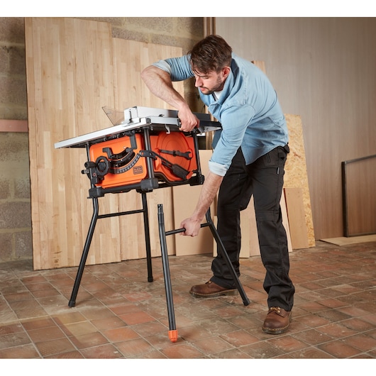 Foto van BLACKDECKER BES720 tafelzaag, geassembleerd door een persoon in een werkplaats, oranje behuizing, zwarte poten.