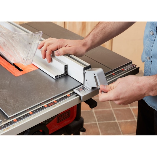 Foto van de BLACKDECKER BES720 tafelzaag in gebruik, handen stellen de geleider en doorzichtige beschermkap af, zijaanzicht.