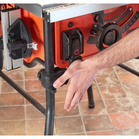 Foto van een BLACKDECKER BES720 tafelzaag, detail met hand die het onderstel op een tegelvloer aanpast.