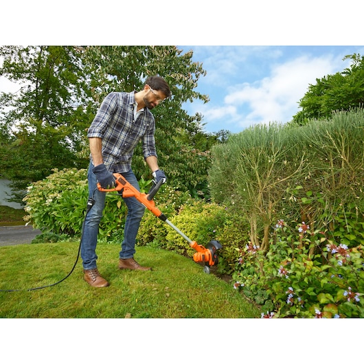 BLACKDECKER BESTA530CM grastrimmer gebruikt in een tuin, oranje en zwart design, buitenomgeving.