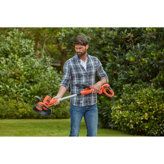 BLACKDECKER BESTA530CM oranje grastrimmer, buiten vastgehouden door persoon met geruit overhemd.