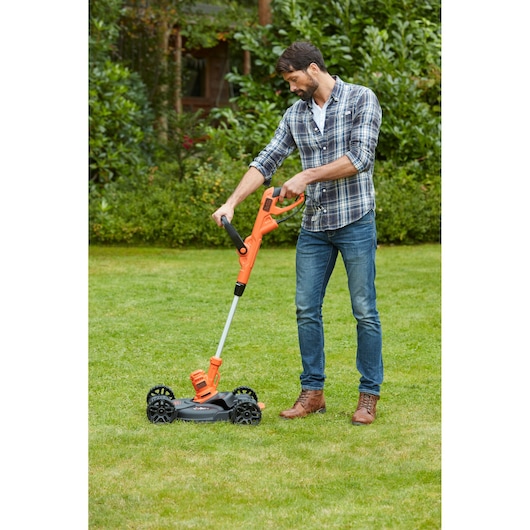 BLACKDECKER BESTA530CM oranje grastrimmer met wielbasis gebruikt buiten op een gazon.