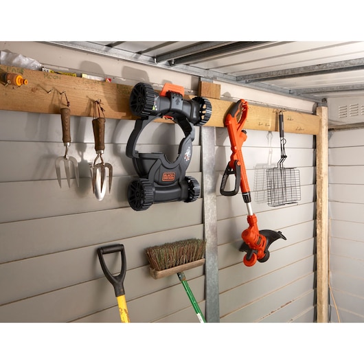 Foto van BLACKDECKER BESTA530CM grasmaaier en trimmer aan de schuurmuur met tuingereedschap.