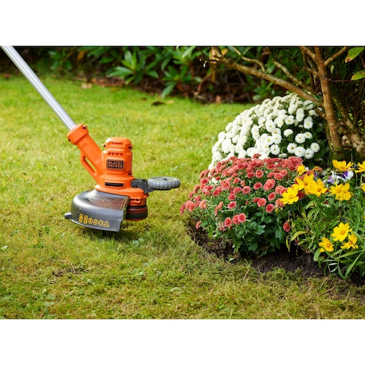 Foto van BLACK+DECKER BESTA530 grastrimmer in gebruik langs het gazon bij een kleurrijk bloemperk.