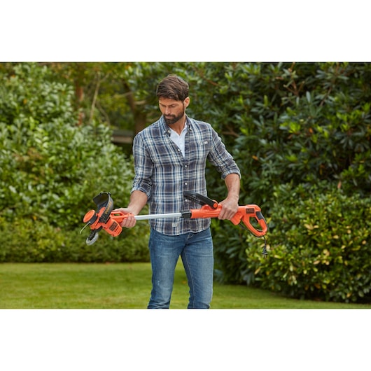 BLACK+DECKER BESTA530 elektrische grastrimmer in oranje en zwart, vastgehouden buiten door persoon in spijkerbroek en geruit shirt.