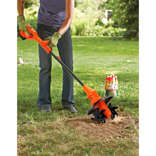 BLACK+DECKER BETL1820L oranje snoerloze tuinfrees in gebruik op grasveld, gebruiker met handschoenen buiten.
