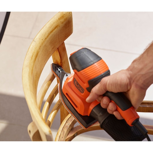 BLACKDECKER BEW200LSA detailschuurmachine gebruikt op houten stoel, oranje en zwart, close-up.