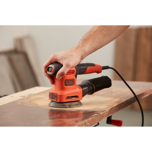 BLACKDECKER BEW200LSA oranje elektrische schuurmachine in gebruik op hout, close-up zijaanzicht.