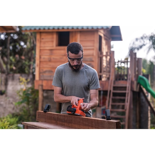 BLACKDECKER BEW712 ponceuse électrique utilisée sur une planche de bois en extérieur, tenue par une personne en t-shirt gris.