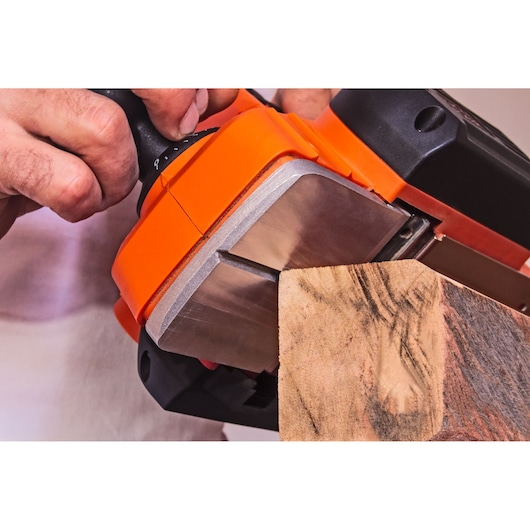 Photo de la ponceuse à bande BLACK+DECKER BEW712 utilisée sur une planche en bois, vue rapprochée.