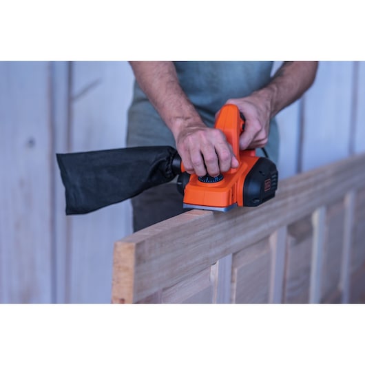 Rabot électrique BLACKDECKER BEW712 utilisé sur une porte en bois, vue latérale, sac à poussière fixé.