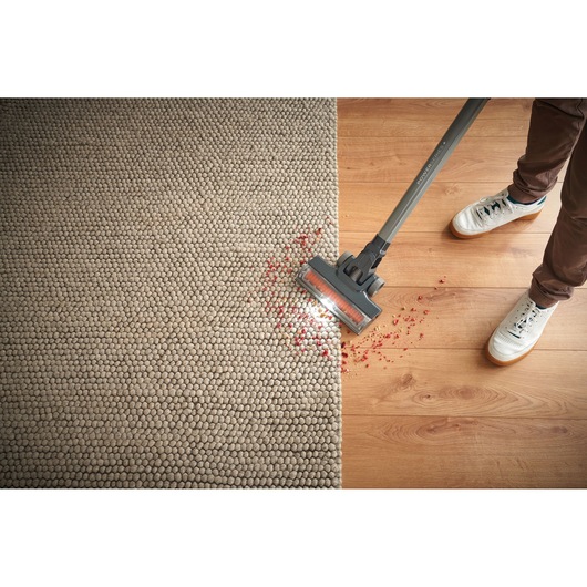 BLACKDECKER BHFEA18D1 aspirateur balai sans fil nettoyant des débris rouges sur tapis et parquet, vue du dessus.