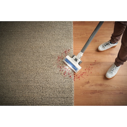 BLACKDECKER BHFEA420J aspirateur balai sans fil nettoyant des débris rouges sur tapis et sol en bois, vue de dessus.