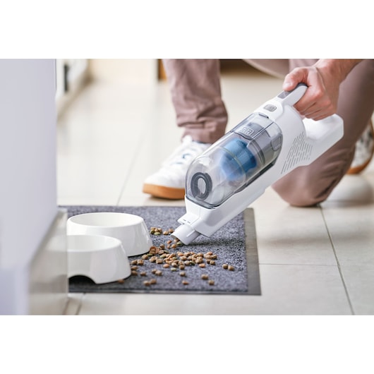 BLACKDECKER BHFEA420J aspirateur à main nettoyant des croquettes pour animaux sur un tapis près des bols.