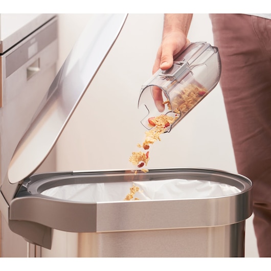 BLACKDECKER BHFEA420J bac à poussière d’aspirateur vidé dans une poubelle de cuisine, vue rapprochée latérale.