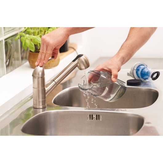 Photo du réservoir à poussière BLACKDECKER BHFEA420J rincé sous un robinet de cuisine près d'un évier inox.