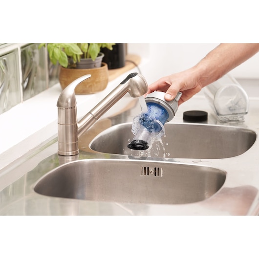Filtre d’aspirateur BLACKDECKER BHFEA420J rincé sous un robinet de cuisine au-dessus d’un évier en acier inoxydable.