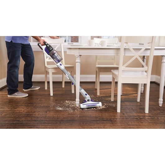 BLACKDECKER BHFEV1825CP snoerloze steelstofzuiger zuigt kruimels op houten vloer bij witte eettafel.