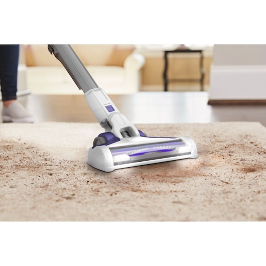 BLACKDECKER BHFEV1825CP draadloze stofzuiger reinigt een vuil tapijt in een woonkamer.