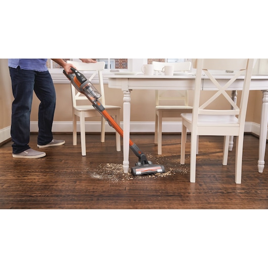 Aspirateur balai sans fil BLACKDECKER BHFEV182B nettoyant des débris sur un sol en bois sous une table à manger.