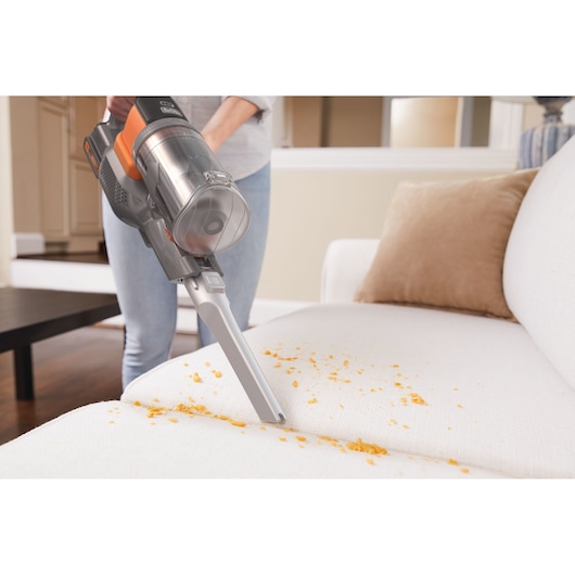 Aspirateur sans fil BLACK+DECKER BHFEV182B nettoyant des miettes sur un canapé blanc dans un salon.