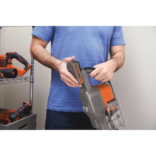 Photo de l’aspirateur sans fil BLACKDECKER BHFEV182B avec insertion de la batterie 18V par une personne.