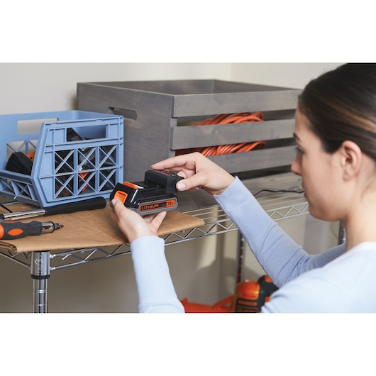 Photo de la batterie lithium 18V BLACKDECKER BHFEV182B utilisée, tenue par une personne près d’étagères.