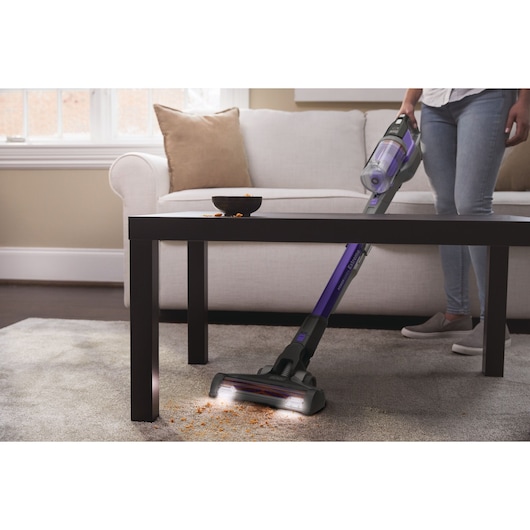 BLACKDECKER BHFEV182CP aspirateur balai nettoyant des miettes sur moquette près d’une table au salon.